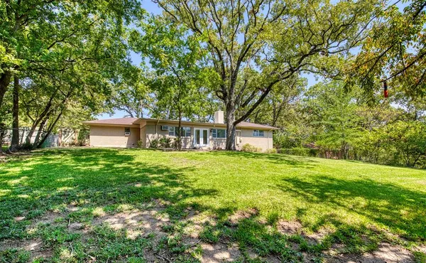 a backyard of a house with table and chairs and large trees
