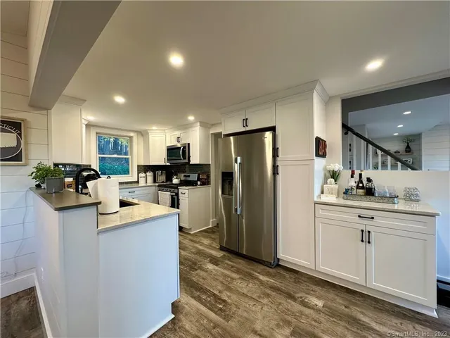 a kitchen with kitchen island a refrigerator a stove a sink cabinets and a dining table with wooden floor