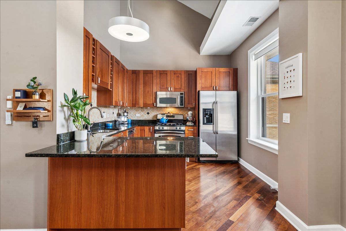 561 West Briar Place, Unit 305 Chicago, IL 60657 - Photo 8 of 23 a kitchen with stainless steel appliances granite countertop a refrigerator a sink dishwasher a stove and a dining table with wooden floor