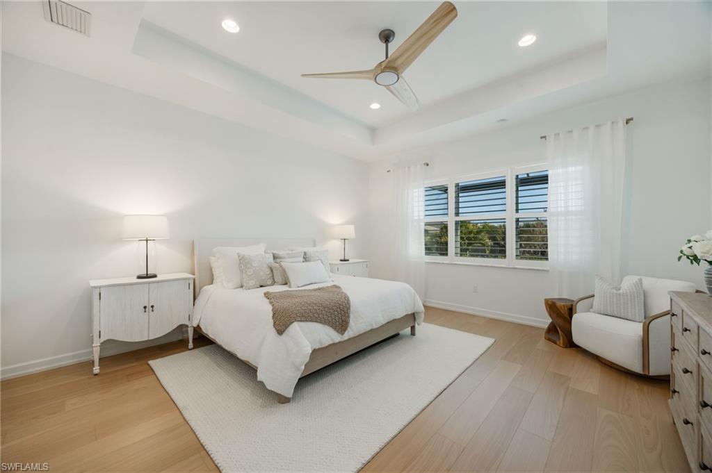 12128 Eucalyptus Way Naples, FL 34120 - Photo 17 of 47 The primary bedroom features a double tray ceiling, wood flooring, and a large picture window overlooking the natural landscape and lake views.
