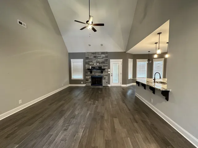 an empty room with wooden floor a ceiling fan a fireplace and windows
