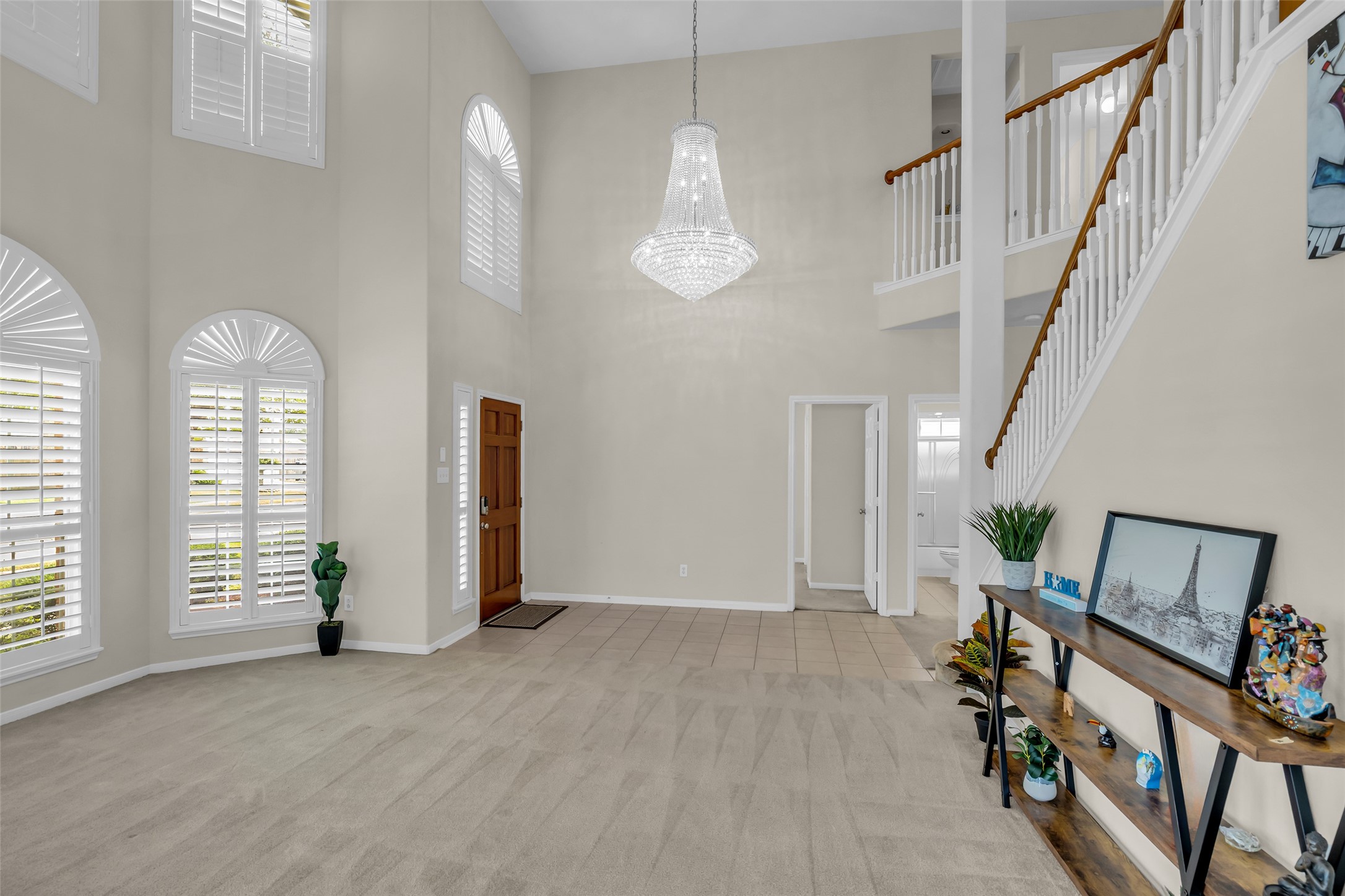 6807 Chapelfield Lane Houston, TX 77049 - Photo 9 of 42 This spacious entryway features high ceilings with a grand chandelier, abundant natural light from arched windows with shutters, and a welcoming staircase. The neutral tones and open layout create an elegant and inviting atmosphere.