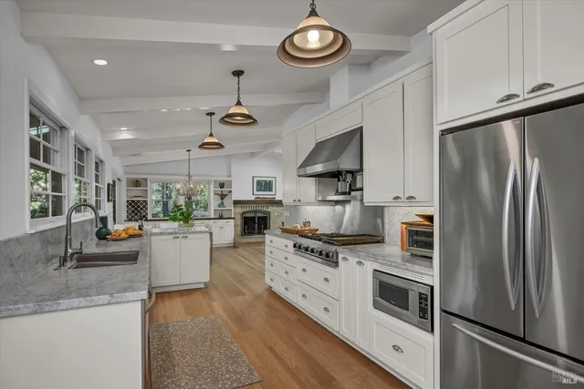 a kitchen with stainless steel appliances a stove a sink dishwasher a refrigerator white cabinets and wooden floor