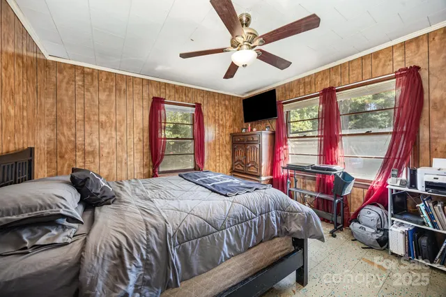 a bedroom with a bed a standing fan and a dresser next to a window