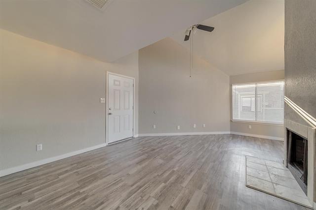 9815 Walnut Street, Unit 212 Dallas, TX 75243 - Photo 3 of 10 Vaulted ceiling living space featuring wood-finish flooring, a white paneled entry door, a ceiling fan, and a tiled fireplace hearth