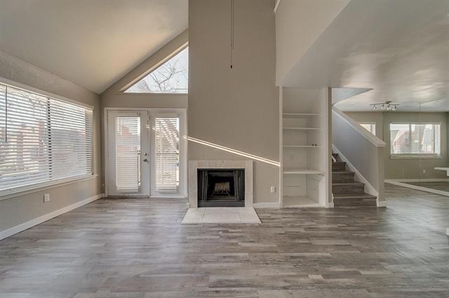 9815 Walnut Street, Unit 212 Dallas, TX 75243 - Photo 5 of 10 Living area featuring vaulted ceilings, wood-finish flooring, a fireplace with a light-toned surround, built-in shelving, and a double-door exterior entry