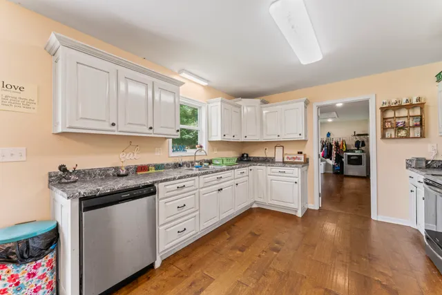 a kitchen with granite countertop a stove top oven a sink dishwasher and white cabinets with wooden floor