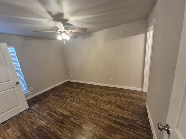a view of an empty room with wooden floor and a ceiling fan
