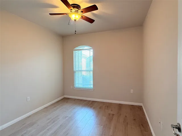 an empty room with wooden floor fan and windows