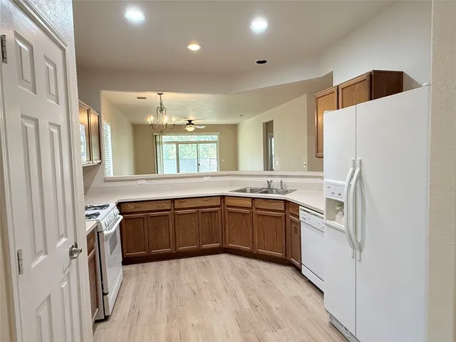 a kitchen with stainless steel appliances granite countertop a refrigerator a sink dishwasher a stove and white cabinets with wooden floor