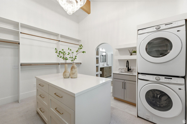 3027 Homestead Road Park City, UT 84098 - Photo 33 of 62 Spacious walk-in closet featuring custom built-in shelving and hanging rods, a central island with drawers, a stacked washer and dryer, and a utility sink with a matte black faucet