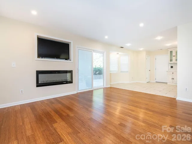 a view of an empty room with wooden floor and a kitchen