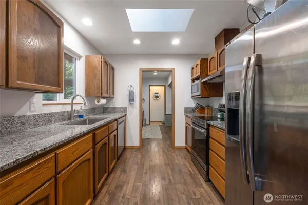 a kitchen with stainless steel appliances granite countertop a refrigerator a sink dishwasher a stove and white countertops with wooden floor