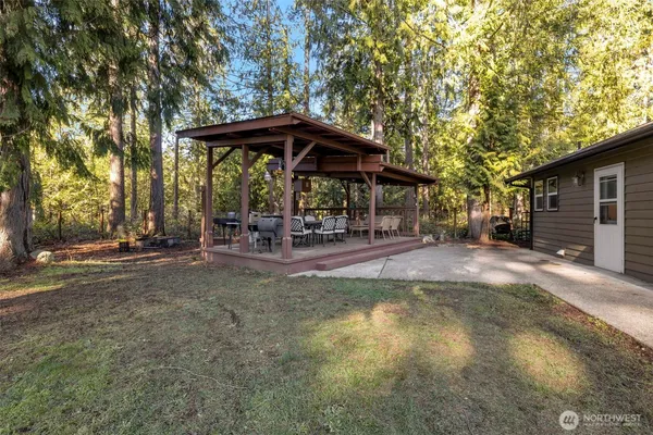 a view of a patio with table and chairs under an umbrella with large trees