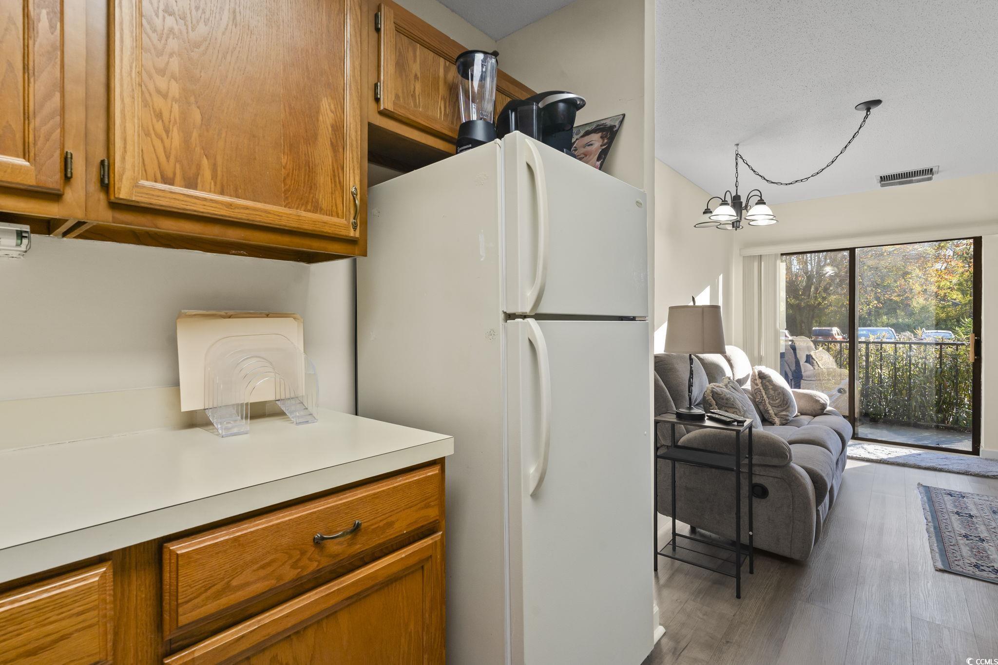 5001 Little River Road, Unit W106 Myrtle Beach, SC 29577 - Photo 8 of 28 Kitchen with brown cabinetry, freestanding refrigerator, light countertops, a chandelier, and a textured ceiling