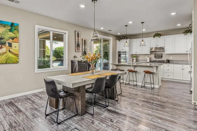 a dining hall with stainless steel appliances granite countertop a stove a refrigerator a kitchen island a dining table and chairs with wooden floor