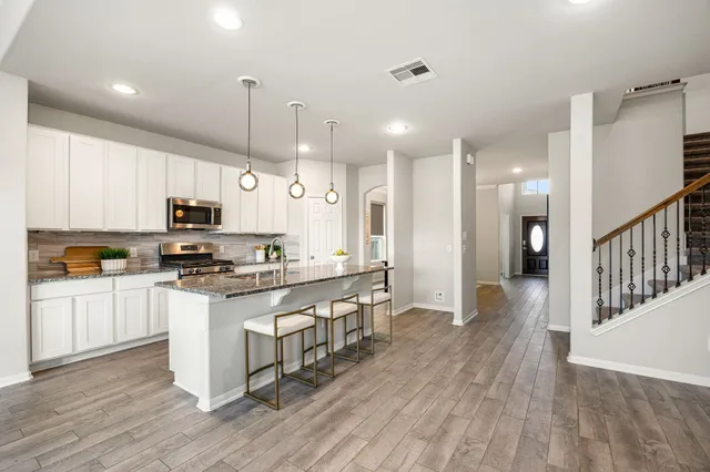 a kitchen with stainless steel appliances kitchen island granite countertop a stove a sink a refrigerator and white cabinets with wooden floor