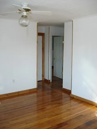 a view of an empty room with wooden floor and a ceiling fan