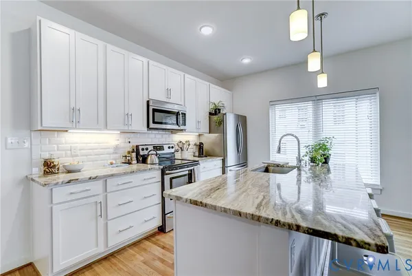a kitchen with granite countertop a sink stainless steel appliances and white cabinets