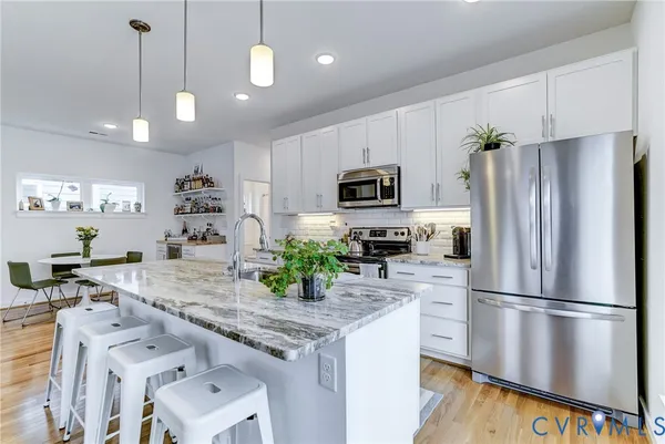 a kitchen with kitchen island granite countertop stainless steel appliances a refrigerator a stove a sink cabinets and a dining table