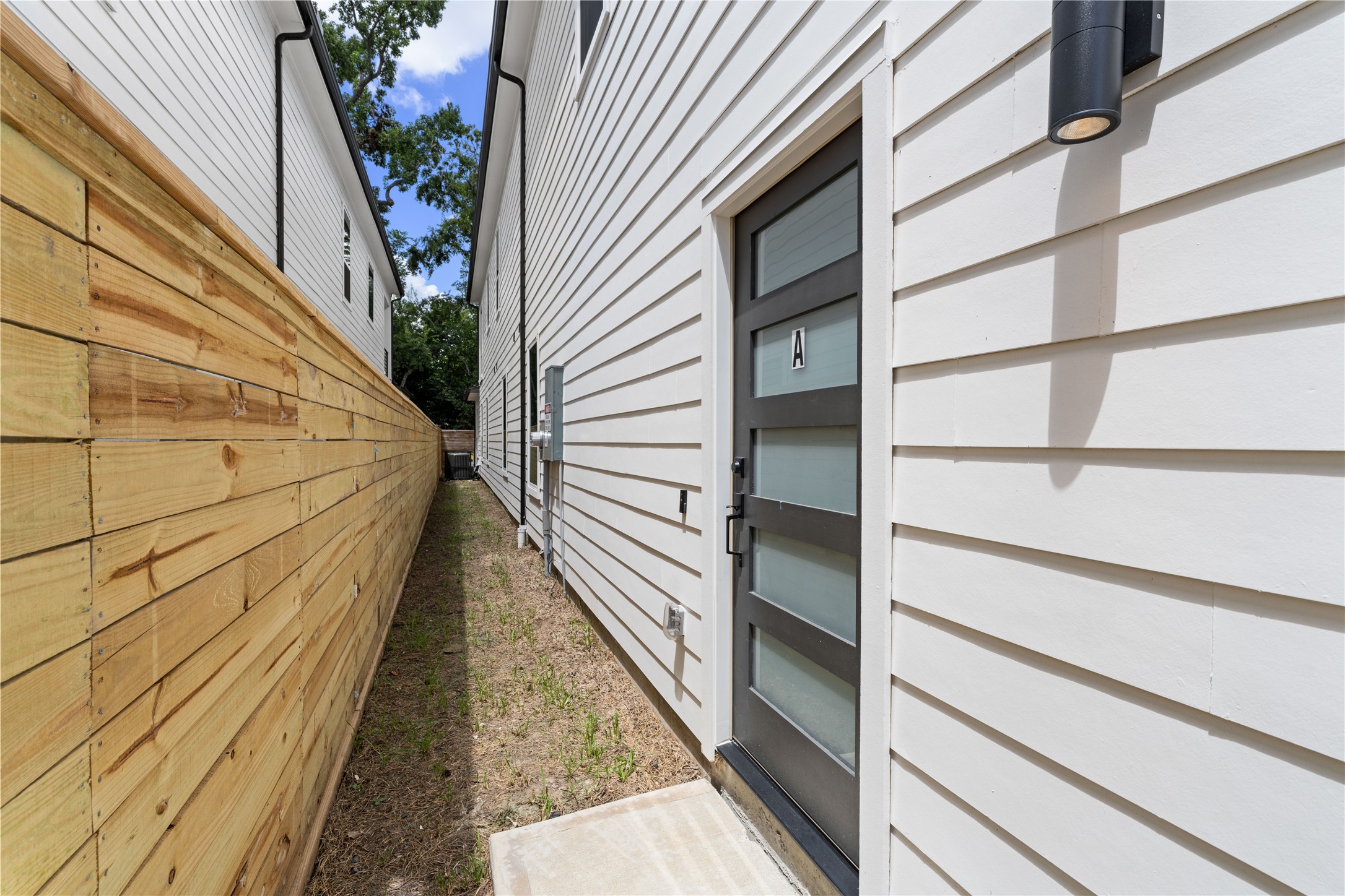 7319 Laura Koppe Road Houston, TX 77028 - Photo 22 of 42 Modern side entrance with sleek panel door, bordered by a wooden privacy fence, offering a clean and private entryway.