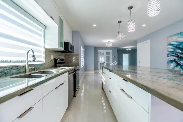 a large kitchen with granite countertop a large counter top a sink stainless steel appliances and cabinets