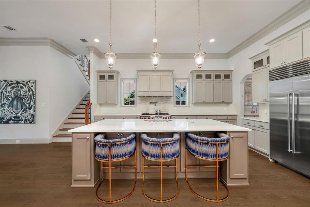 12114 Prestonridge Road Dallas, TX 75230 - Photo 20 of 40 Contemporary kitchen featuring an oversized island with seating, pendant lighting, stainless steel appliances, white cabinetry, and wood-finish flooring