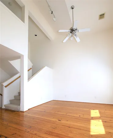 a view of an empty room with wooden floor and a ceiling fan