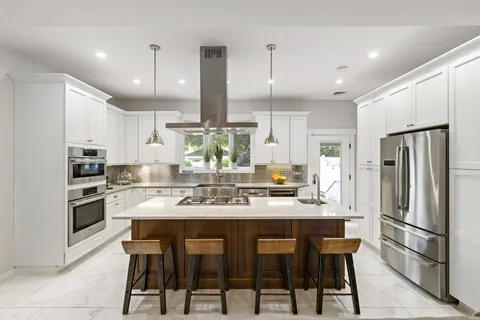 a kitchen with stainless steel appliances kitchen island granite countertop a stove a refrigerator a oven a sink with a dining table and chairs