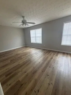 an empty room with wooden floor ceiling fan and windows