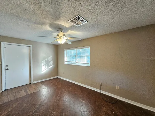 an empty room with wooden floor fan and windows