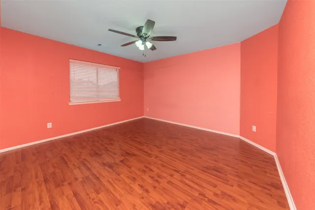 a view of an empty room with wooden floor and a ceiling fan