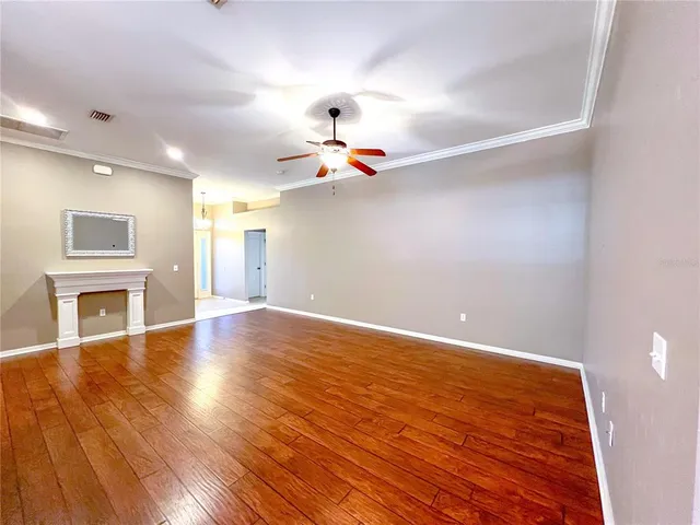 a view of an empty room with chandelier fan and wooden floor