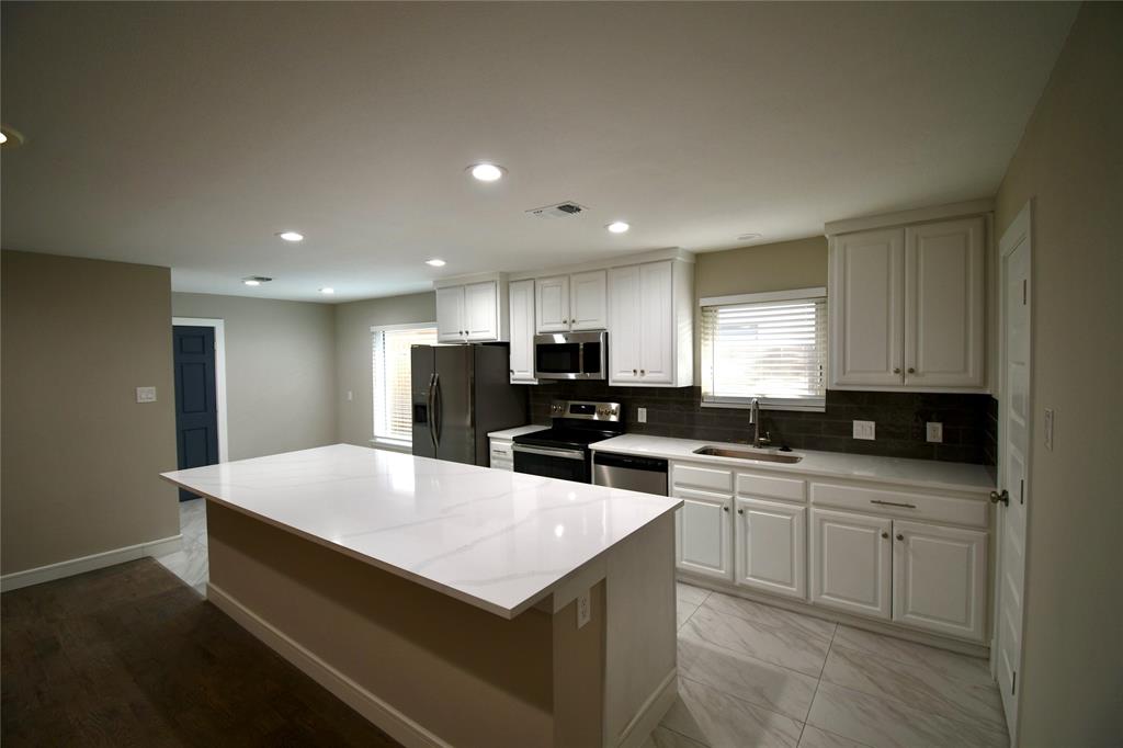 a large kitchen with kitchen island a sink dishwasher a stove a refrigerator and white cabinets with wooden floor