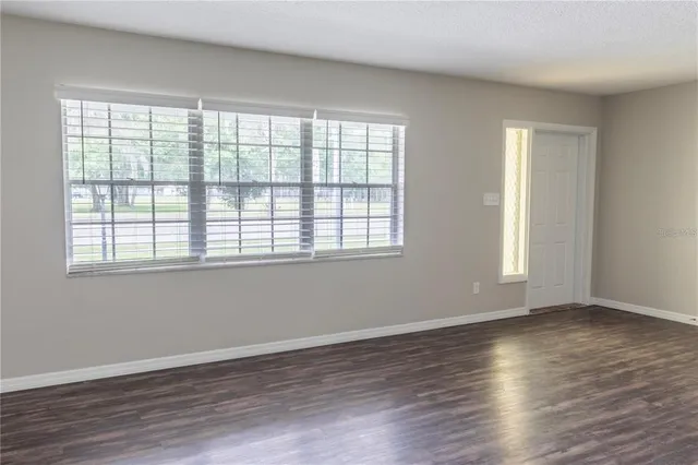 a view of an empty room with wooden floor and a window