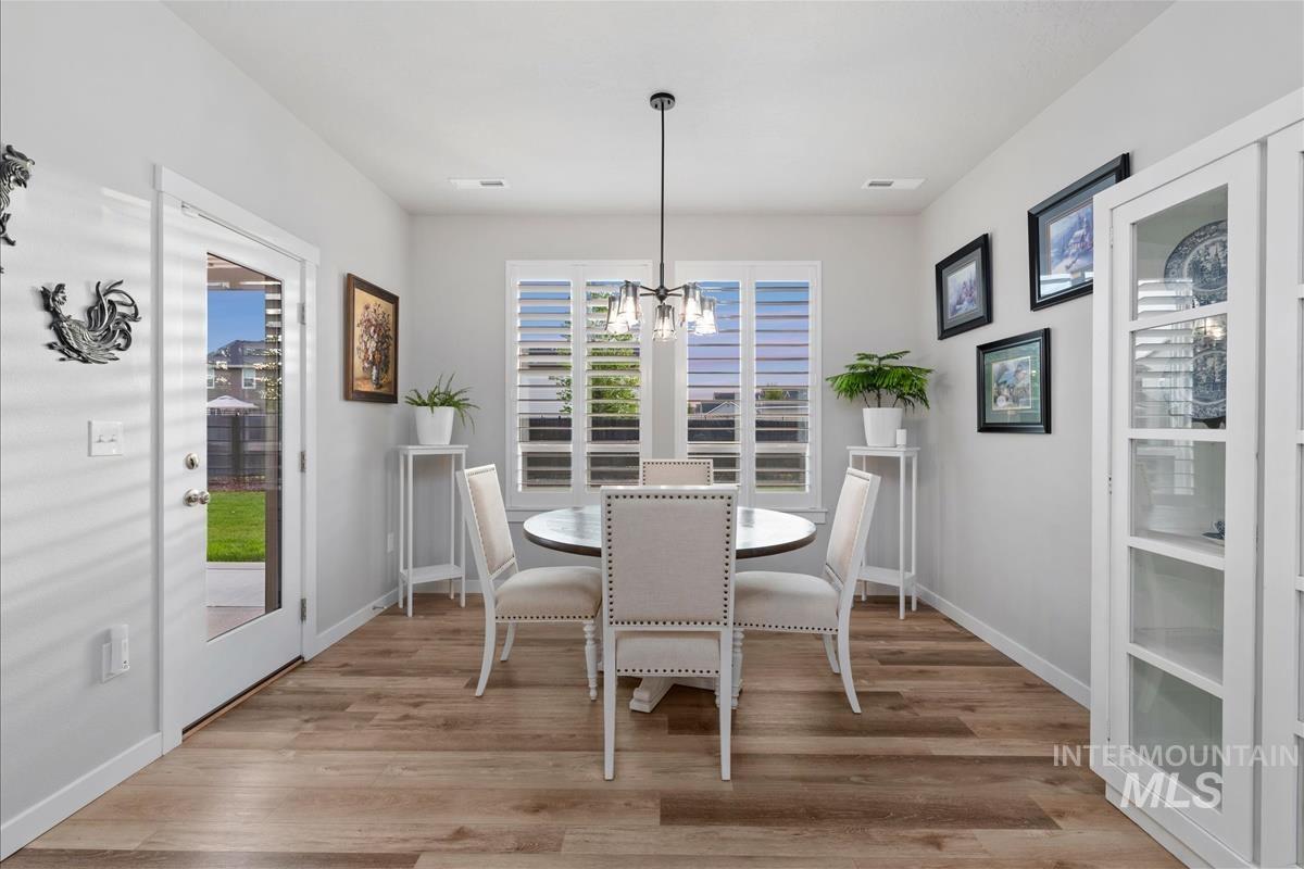 15451 Lutsen Avenue Caldwell, ID 83607 - Photo 18 of 39 Dining area featuring wood-finish flooring, a contemporary chandelier, a window with louvered shutters, a built-in display cabinet, and a glass-paneled exterior door