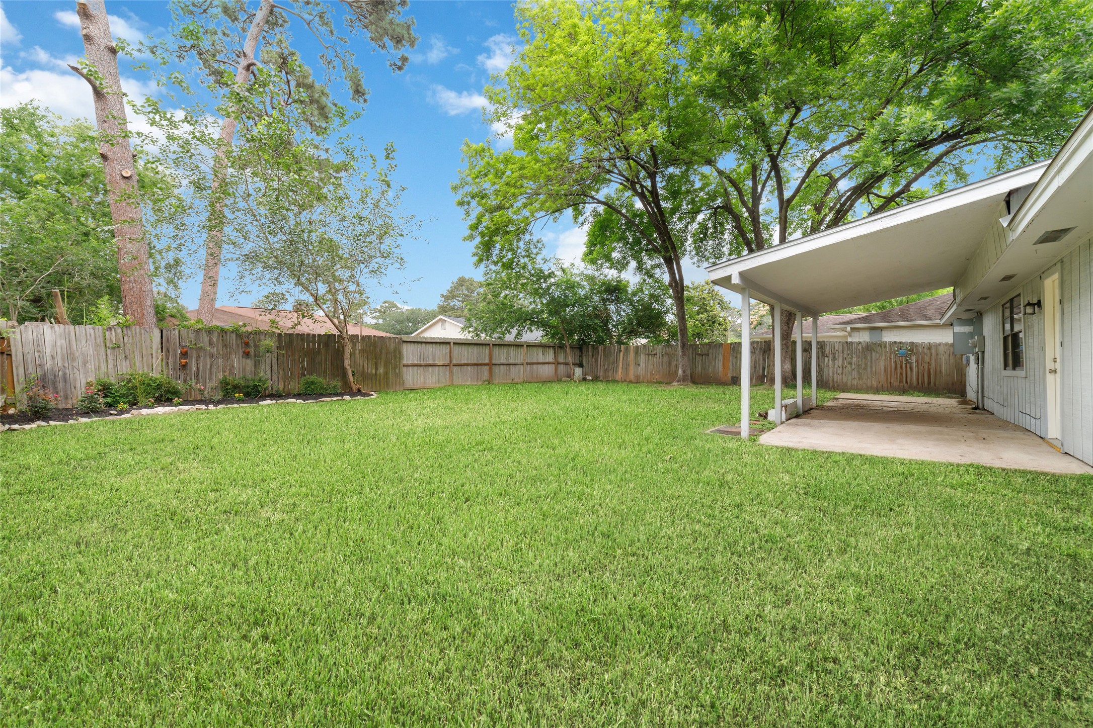 5023 Monteith Drive Spring, TX 77373 - Photo 19 of 20 Spacious backyard with open green space and a covered patio, offering a seamless transition from indoor living to outdoor relaxation under a canopy of trees.