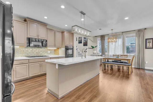 a kitchen with stainless steel appliances granite countertop a stove a sink a refrigerator and white cabinets with wooden floor