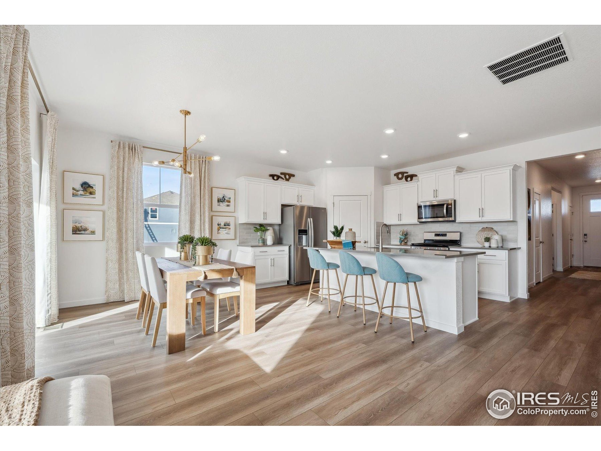 2207 Crosswind Street Fort Lupton, CO 80621 - Photo 4 of 26 a kitchen with a dining table chairs wooden floor cabinets and stainless steel appliances