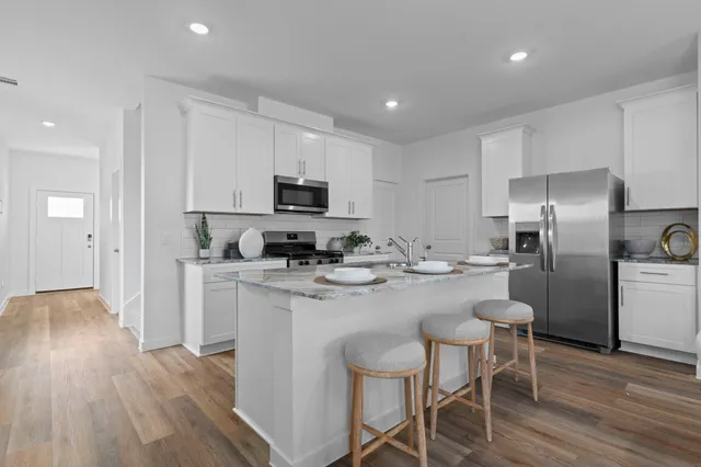 a kitchen with kitchen island a refrigerator stove a sink and white cabinets with wooden floor