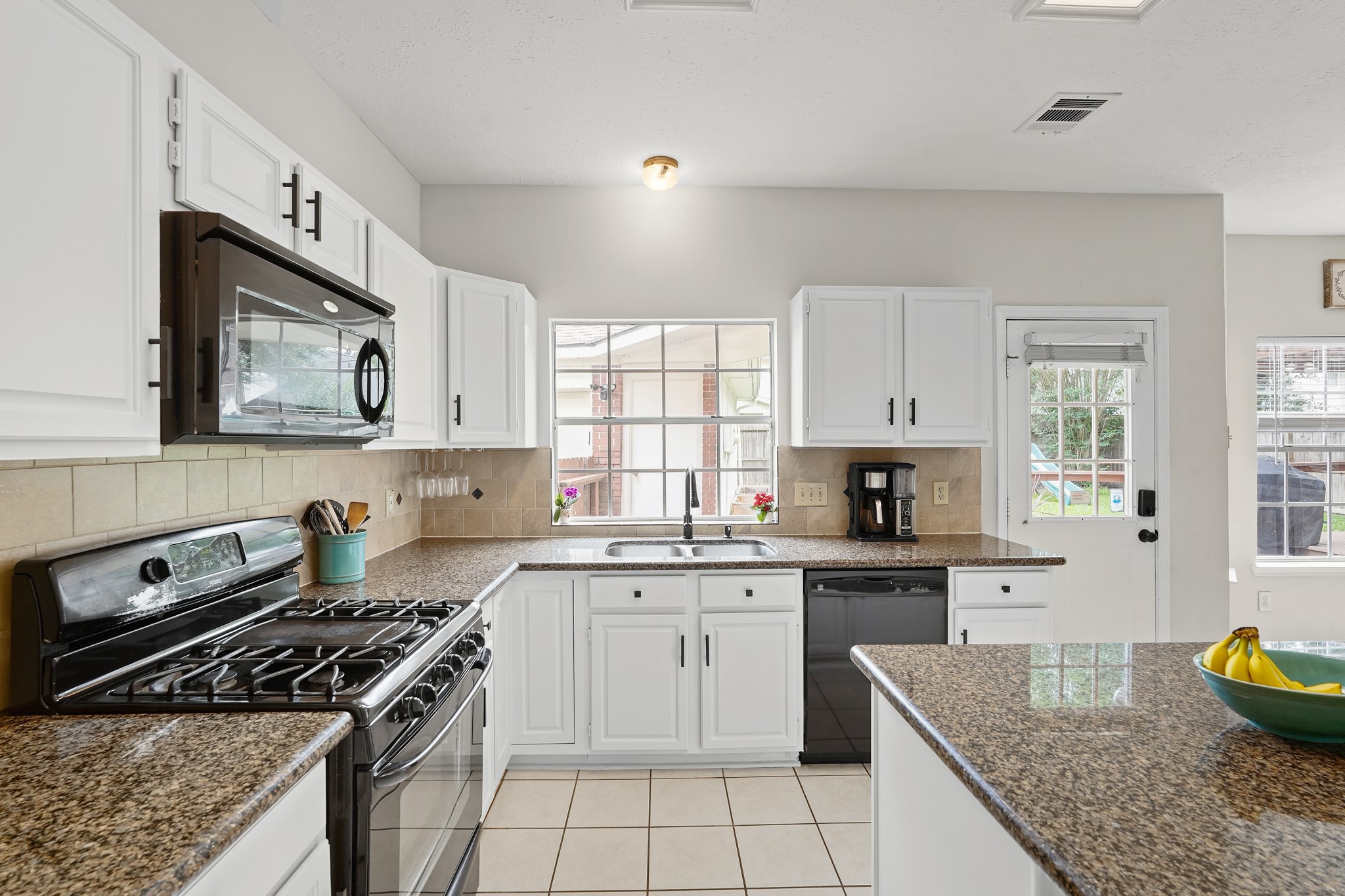 16114 Kintyre Point Road Houston, TX 77095 - Photo 21 of 44 Bright and inviting kitchen featuring granite countertops, white cabinetry, and modern appliances. A large window and glass door provide ample natural light, enhancing the open and airy feel. Perfect for both cooking and entertaining.