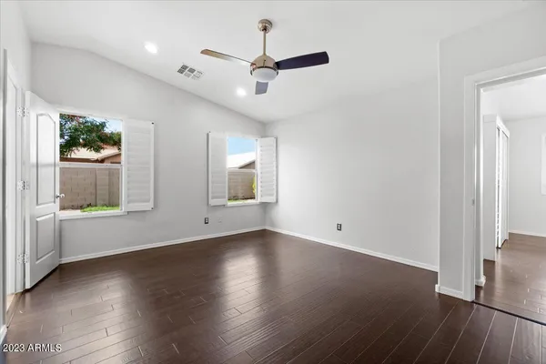an empty room with wooden floor chandelier fan and windows