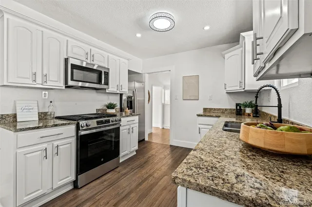 a kitchen with stainless steel appliances granite countertop a stove top oven a sink dishwasher and a refrigerator with wooden floor