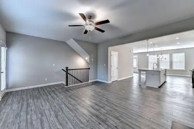 a view of an empty room with wooden floor a ceiling fan and windows