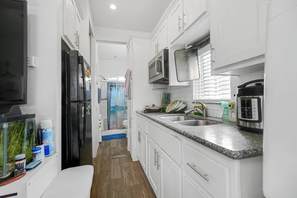 a kitchen with stainless steel appliances granite countertop a refrigerator a sink dishwasher and white cabinets with wooden floor