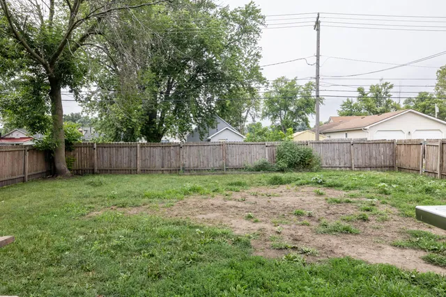 a view of a backyard with wooden fence and large trees