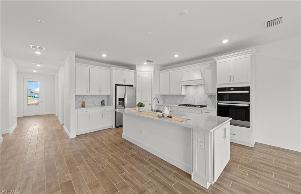 15629 Northridge Road Punta Gorda, FL 33982 - Photo 4 of 26 a large white kitchen with a stove a sink a refrigerator and white cabinets with wooden floor