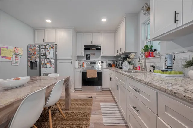 a kitchen with stainless steel appliances kitchen island granite countertop a sink dishwasher a stove and white cabinets with wooden floor