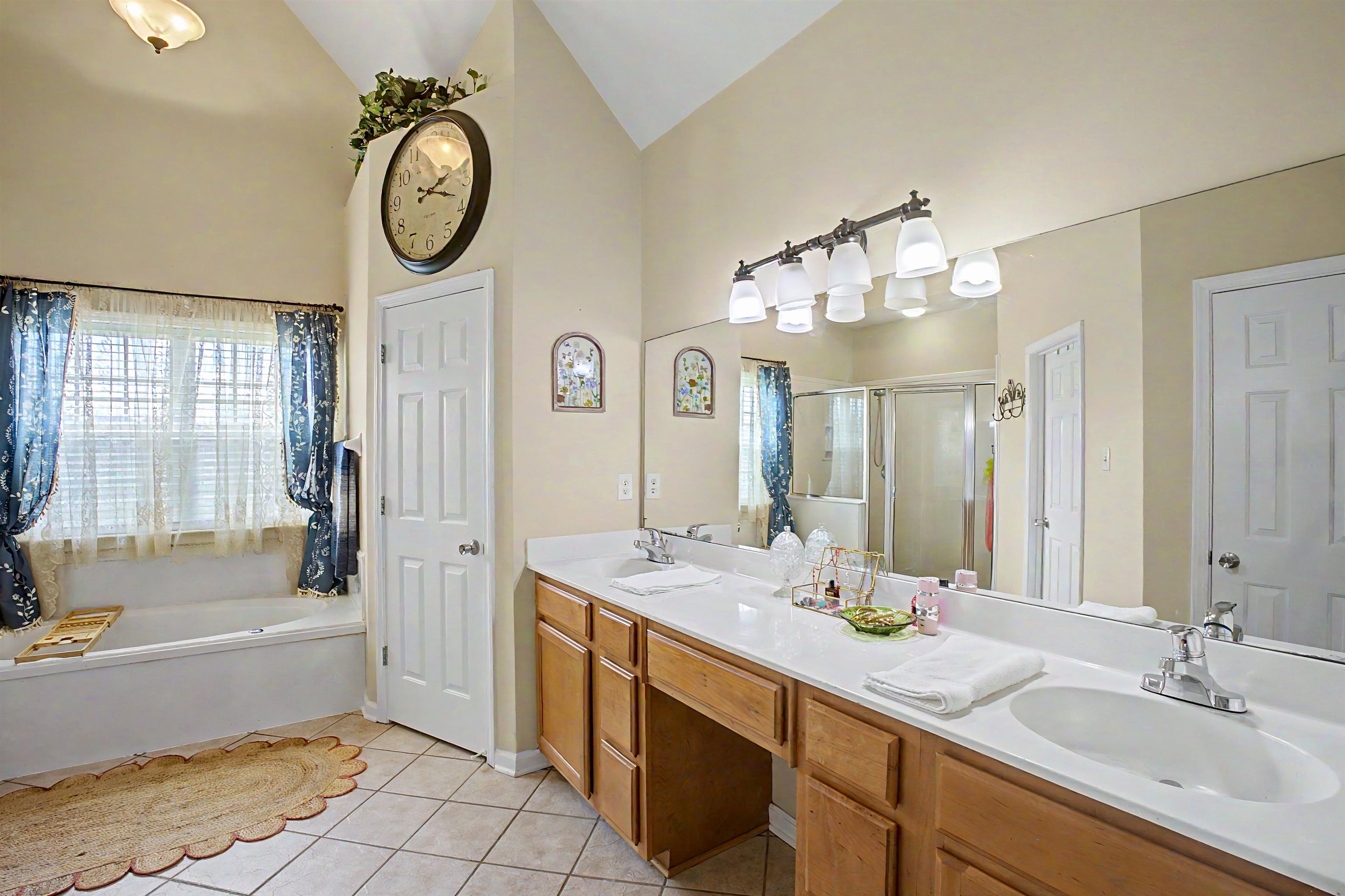134 Rembert Drive Atoka, TN 38004 - Photo 27 of 38 Bathroom featuring a dual vanity with light-tone wood cabinetry and white countertops, an integrated soaking tub with an exterior window, a glass-enclosed shower, and tile flooring
