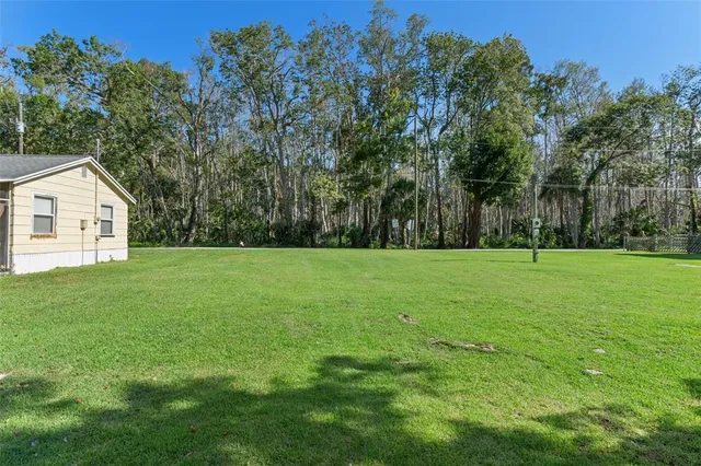 a view of a white house in front of a big yard with plants and large trees